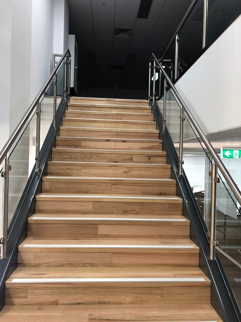 View from bottom of wood staircase in office with metal hand railing and glass panels