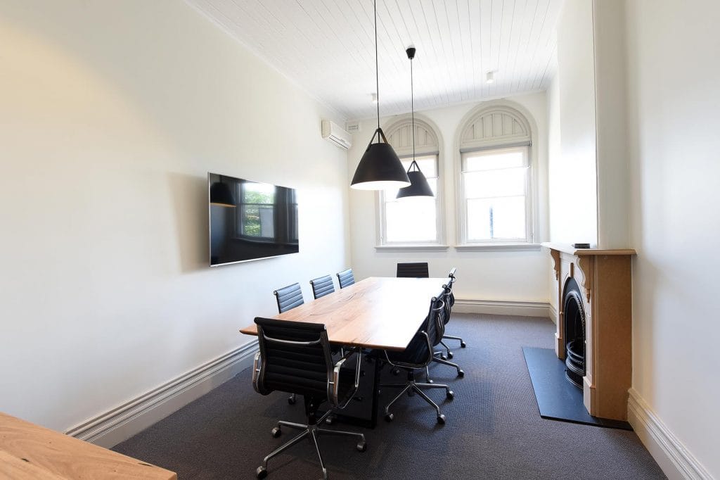 Meeting room with solid wooden table surrounded by black office chairs and a fireplace to the right